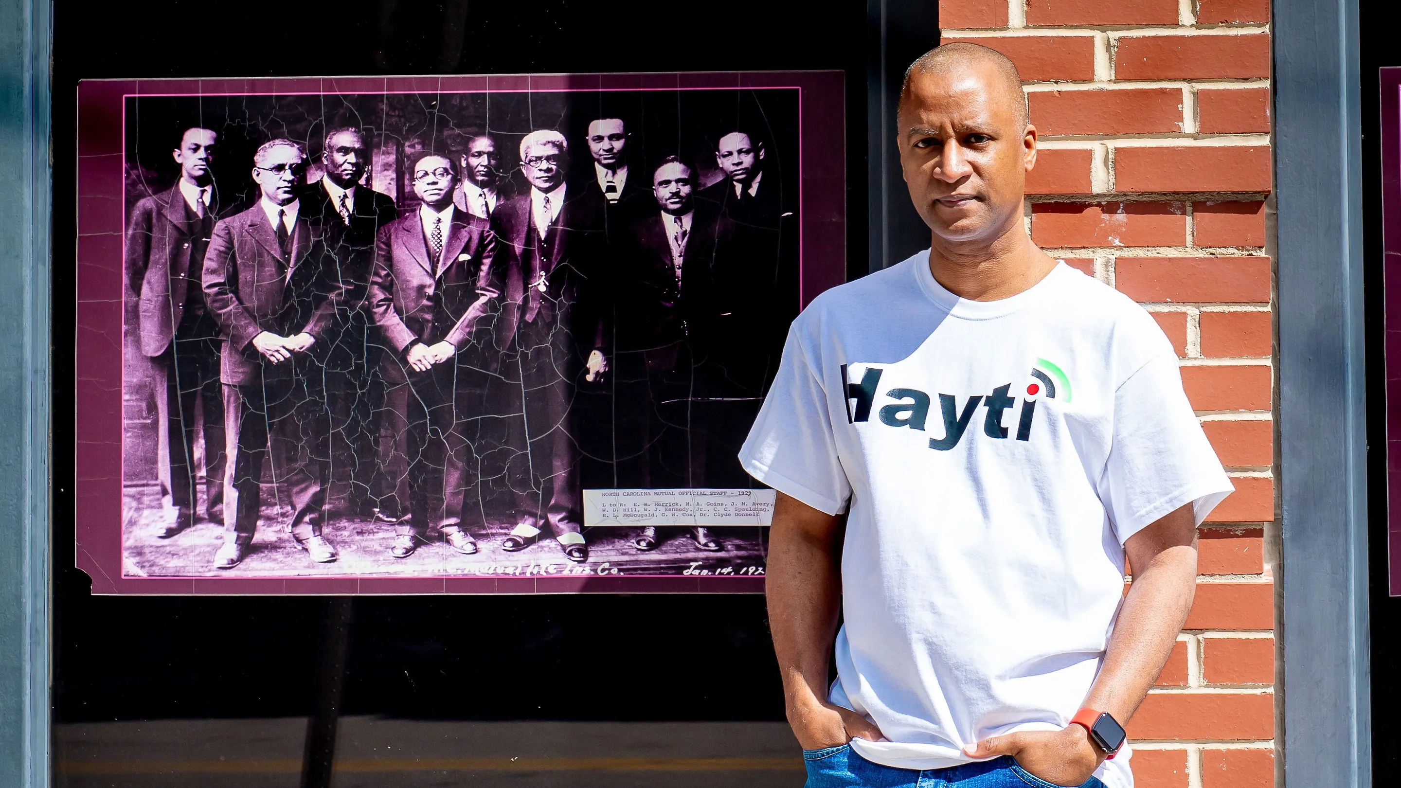 Cary poses next to a vintage portrait of Black leaders, representing a modern digital Black Wall Street